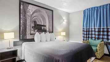 Quarto de hotel com uma cama grande, duas luminárias de cabeceira, uma luz na parede, uma cortina estampada e um quadro acima da cama.