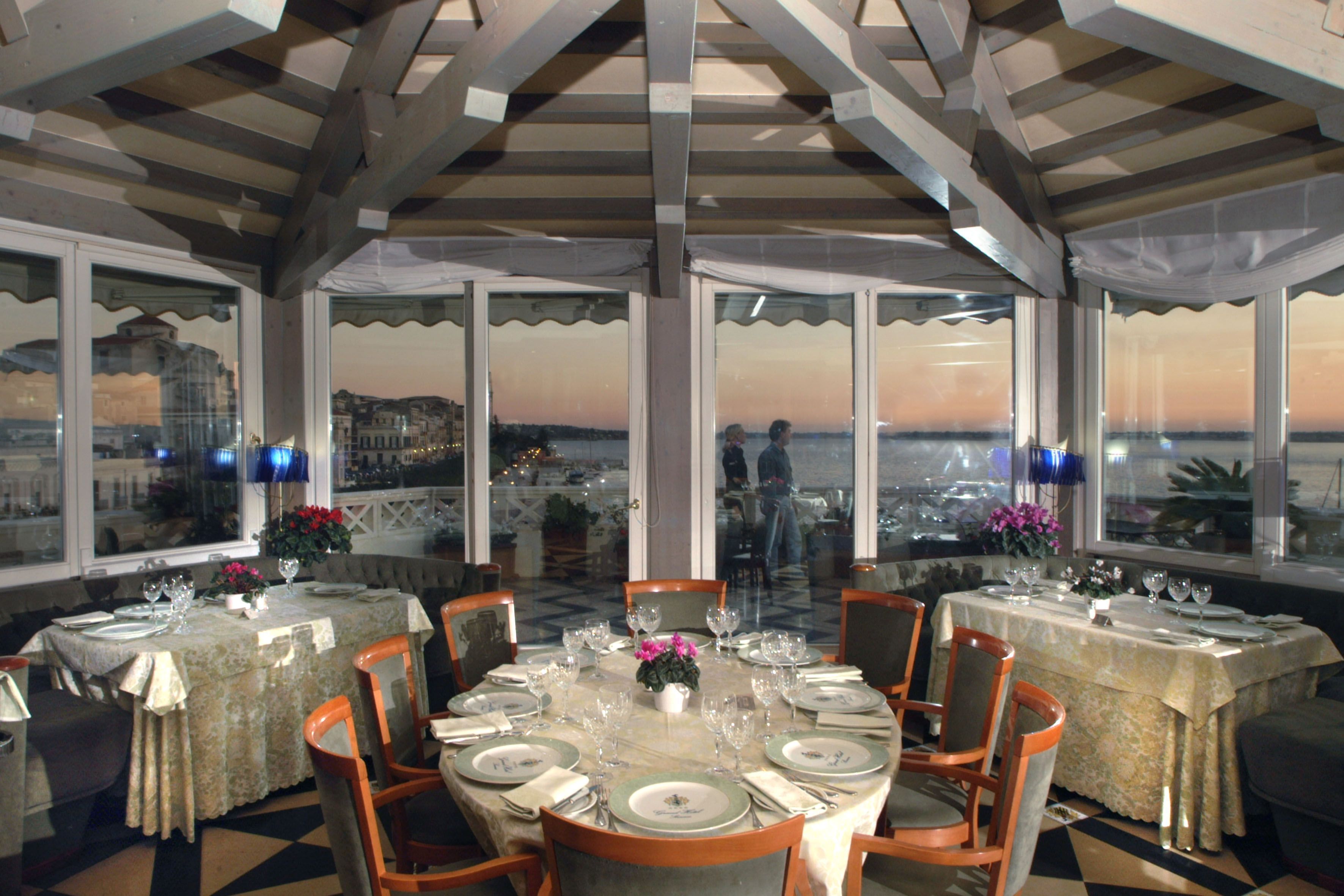 A restaurant with tables set for dining, large windows offering a view of the city, and a covered outdoor area.