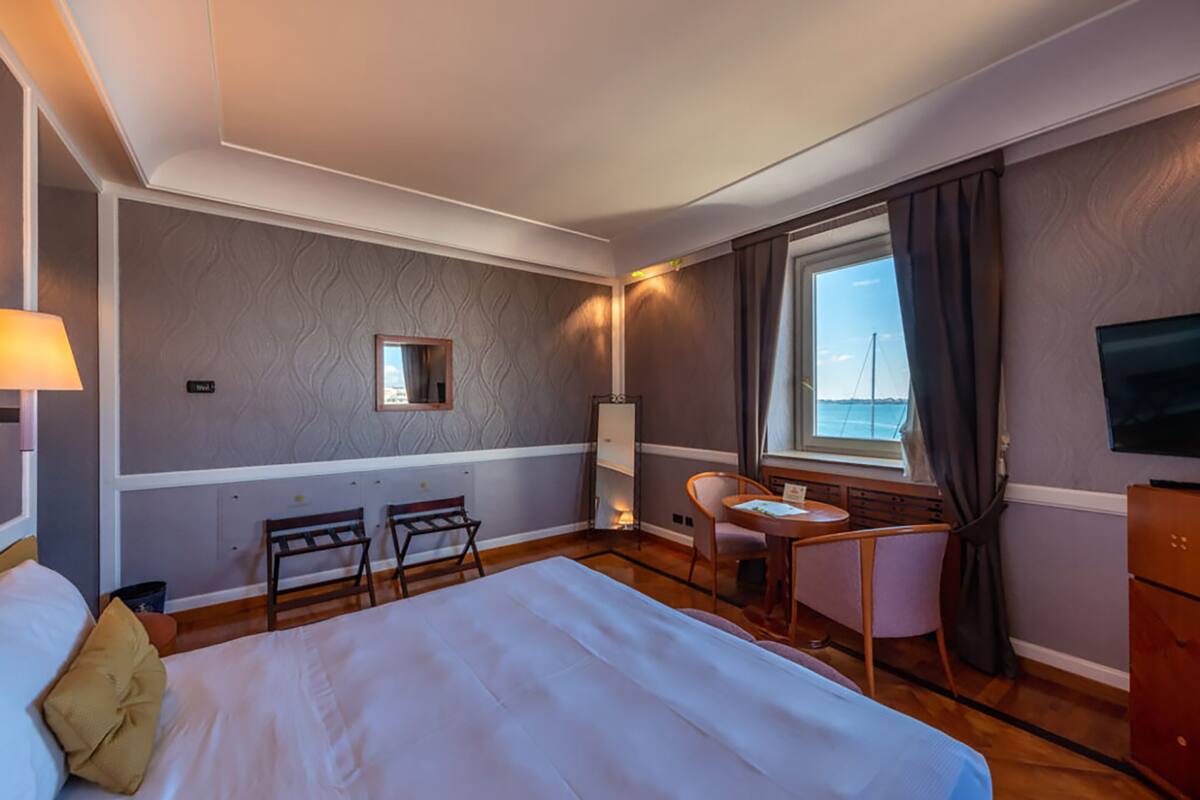 Habitación de hotel con una cama grande, un escritorio, dos sillas, un televisor y una ventana con vistas.