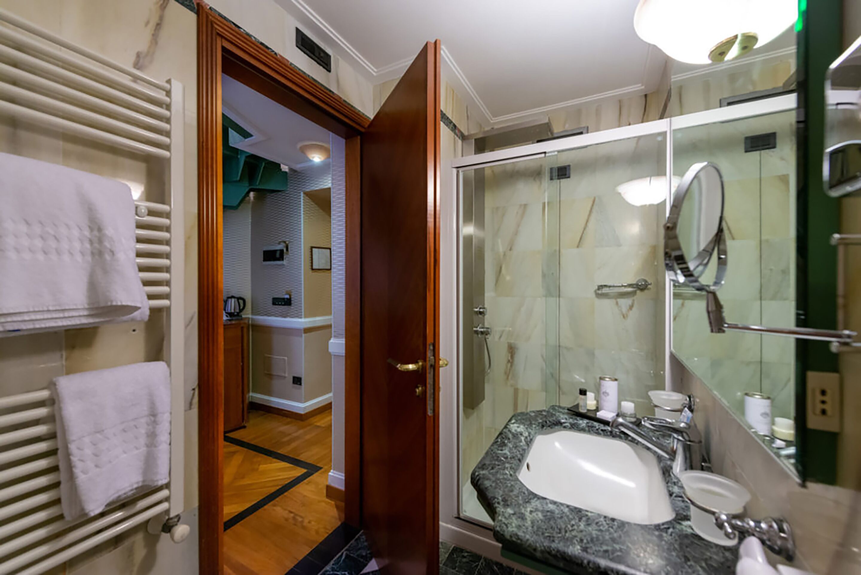 A bathroom with a glass shower enclosure, a sink with a marble countertop, and a mirror.