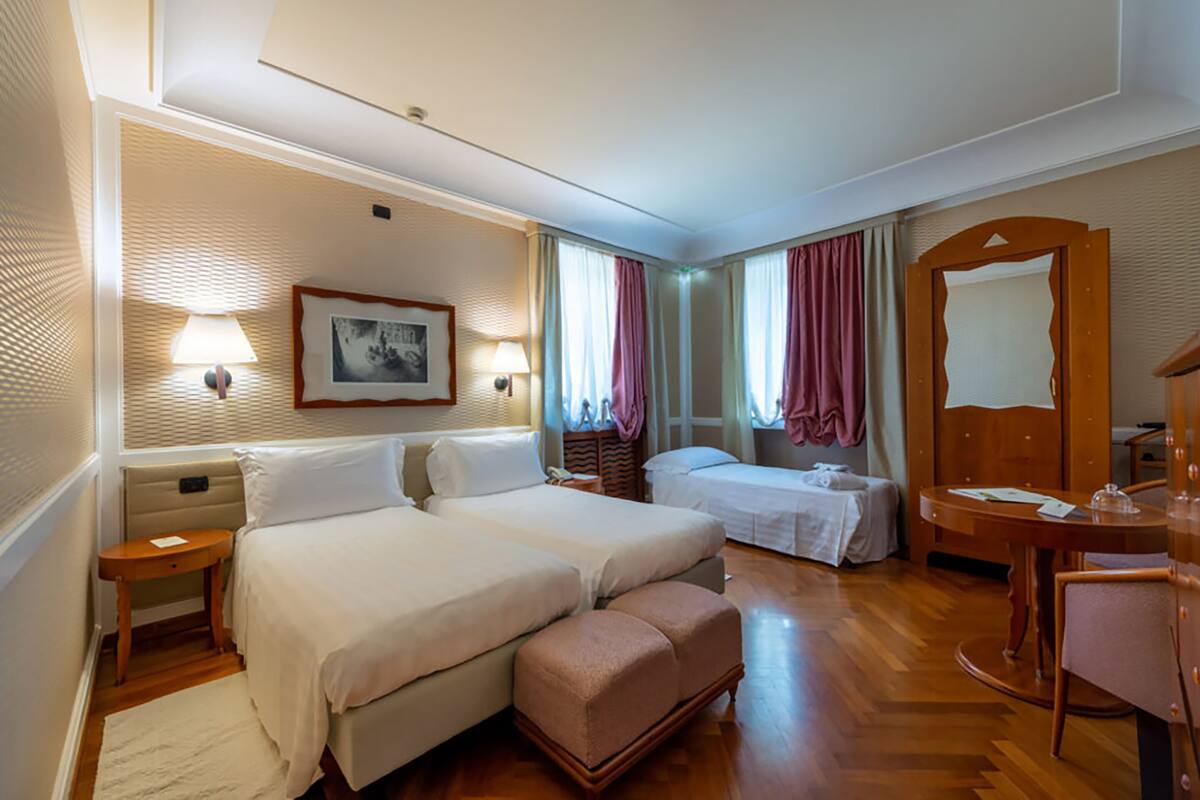 Habitación de hotel con dos camas, piso de madera, una mesita, una silla y un espejo.