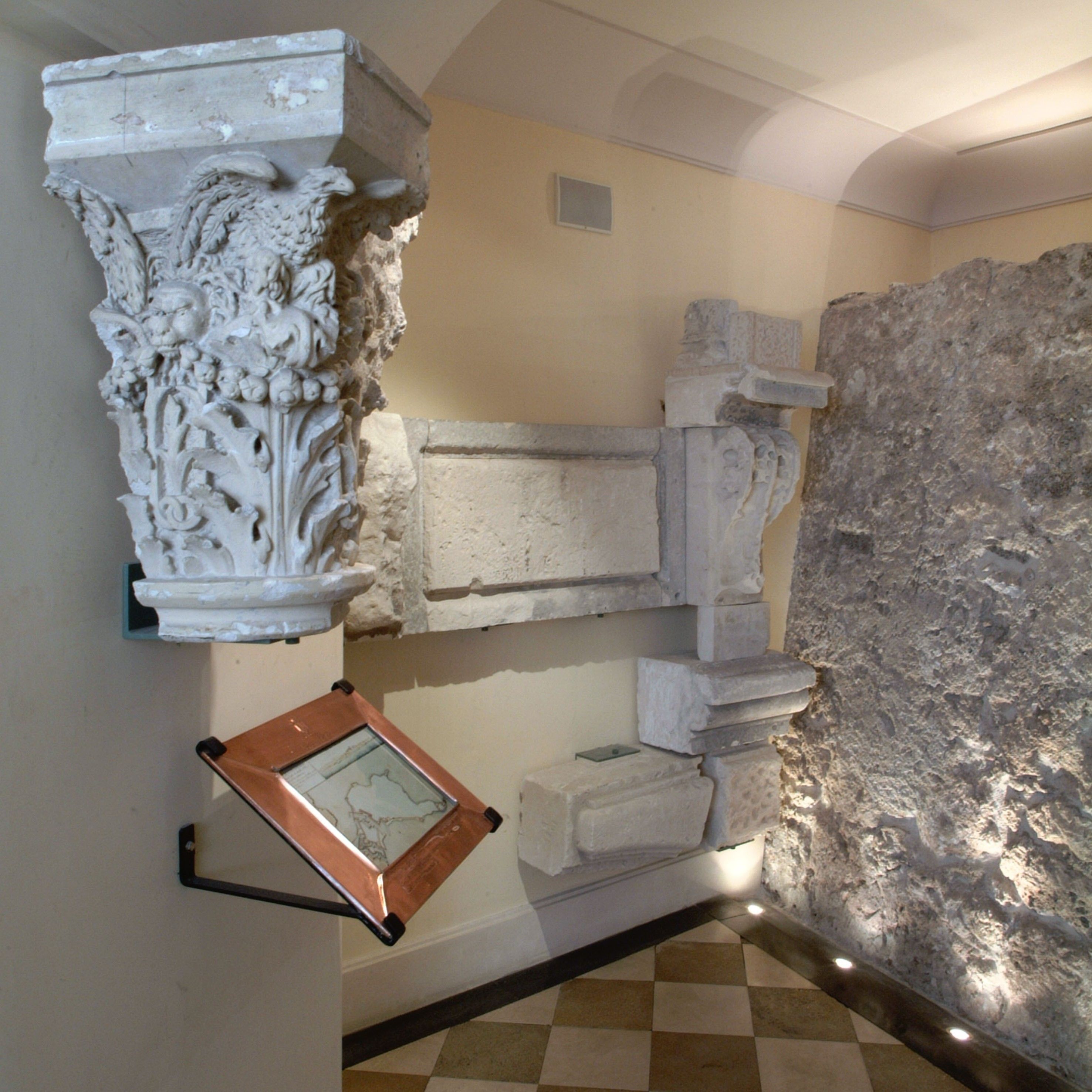 A room with a stone wall, a white decorative column, and a framed map on the wall.
