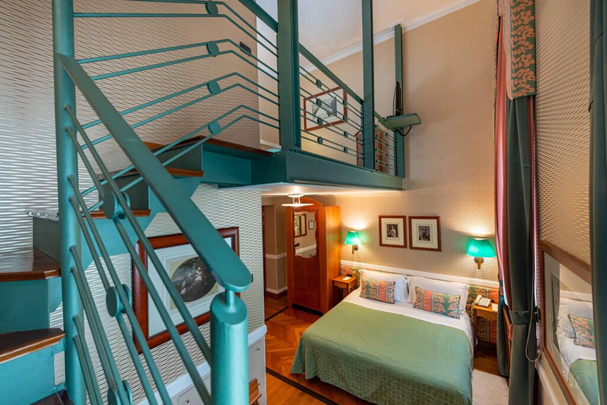 Habitación de hotel con una escalera, una cama con colcha verde, dos lámparas de noche y una mesita de noche.