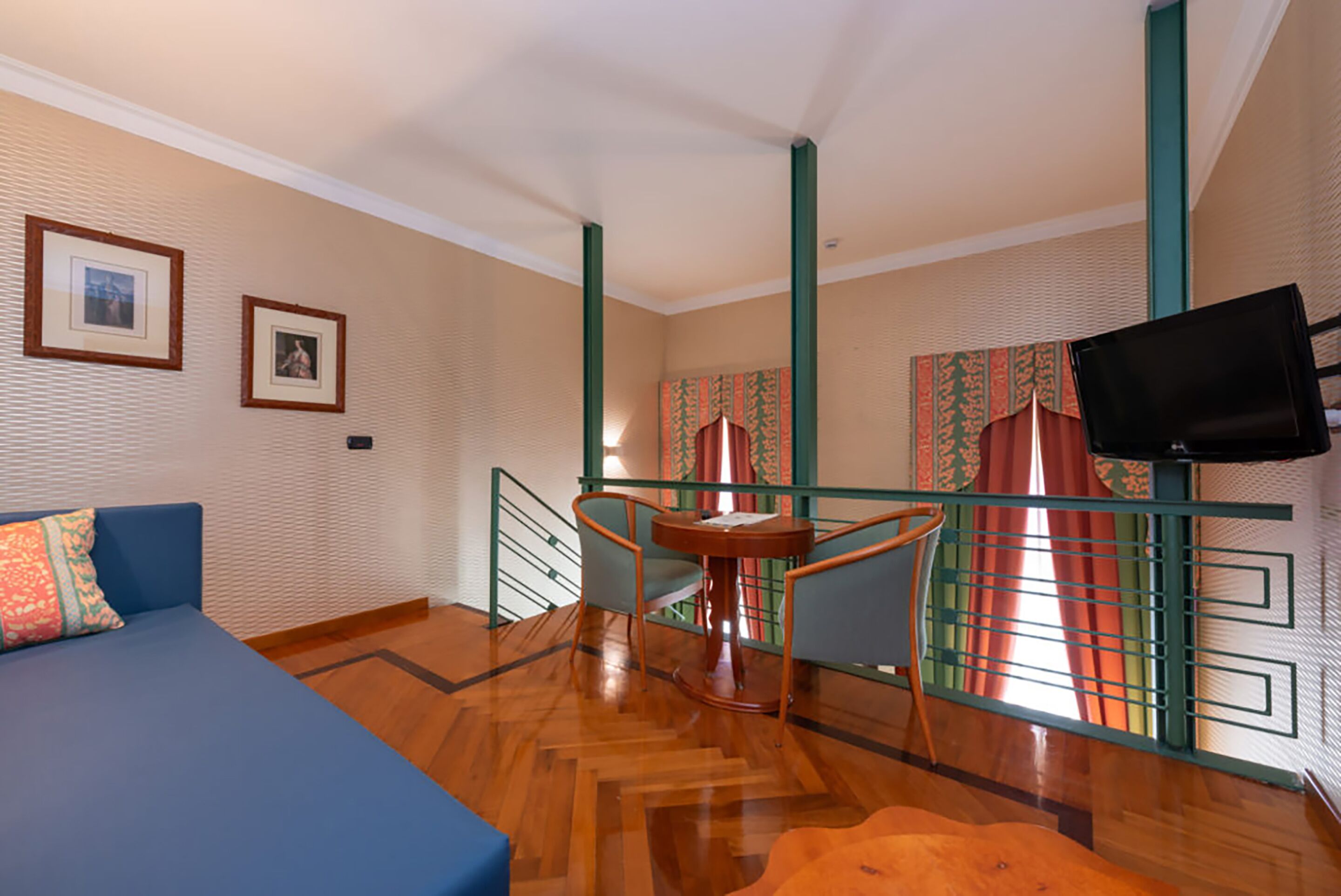 Ein Zimmer mit einem blauen Sofa, einem Holztisch, einem Sessel, einem an der Wand befestigten Fernseher und einer Treppe mit Geländer.