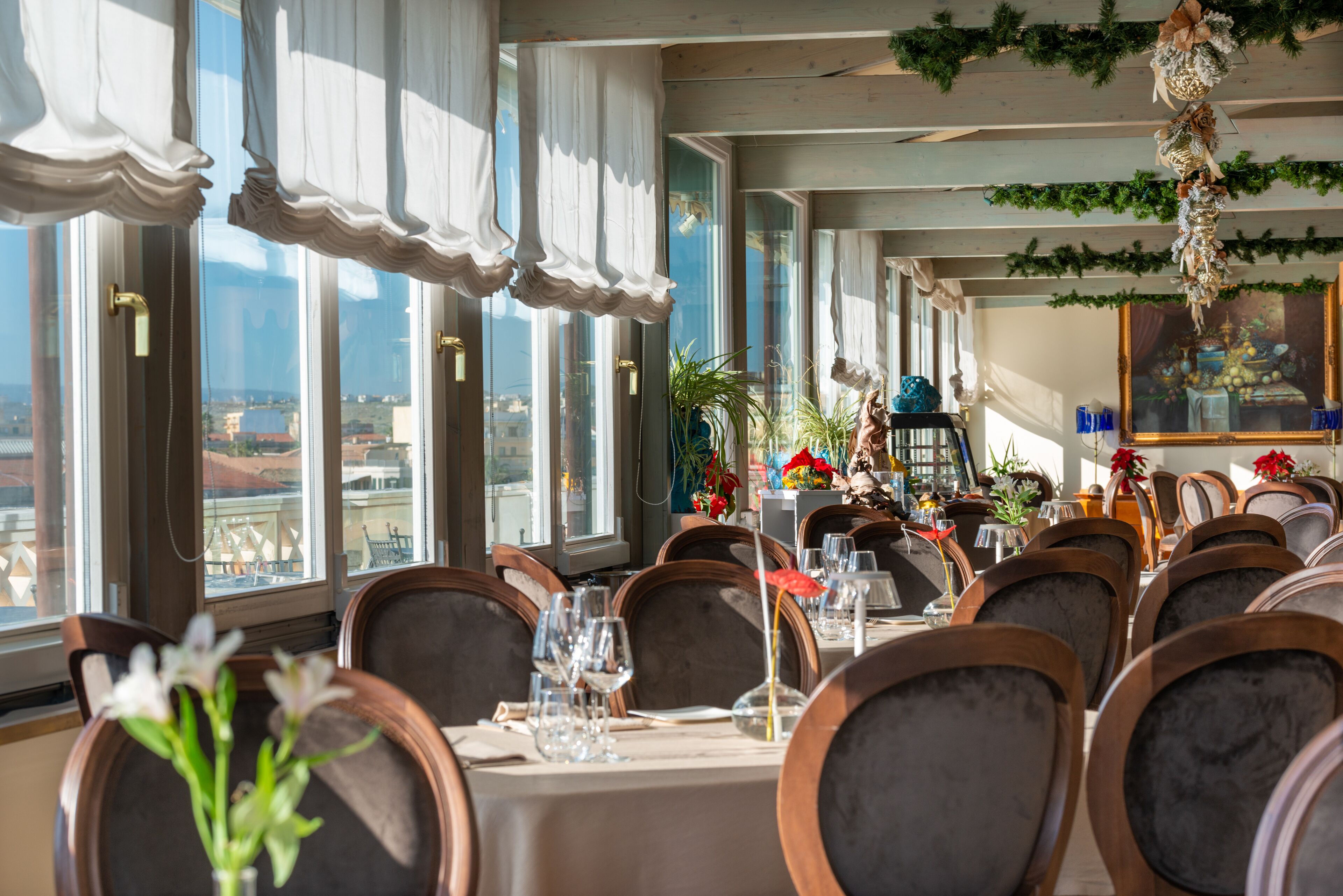 A restaurant with a long table set for dining, large windows, and a view of the city.