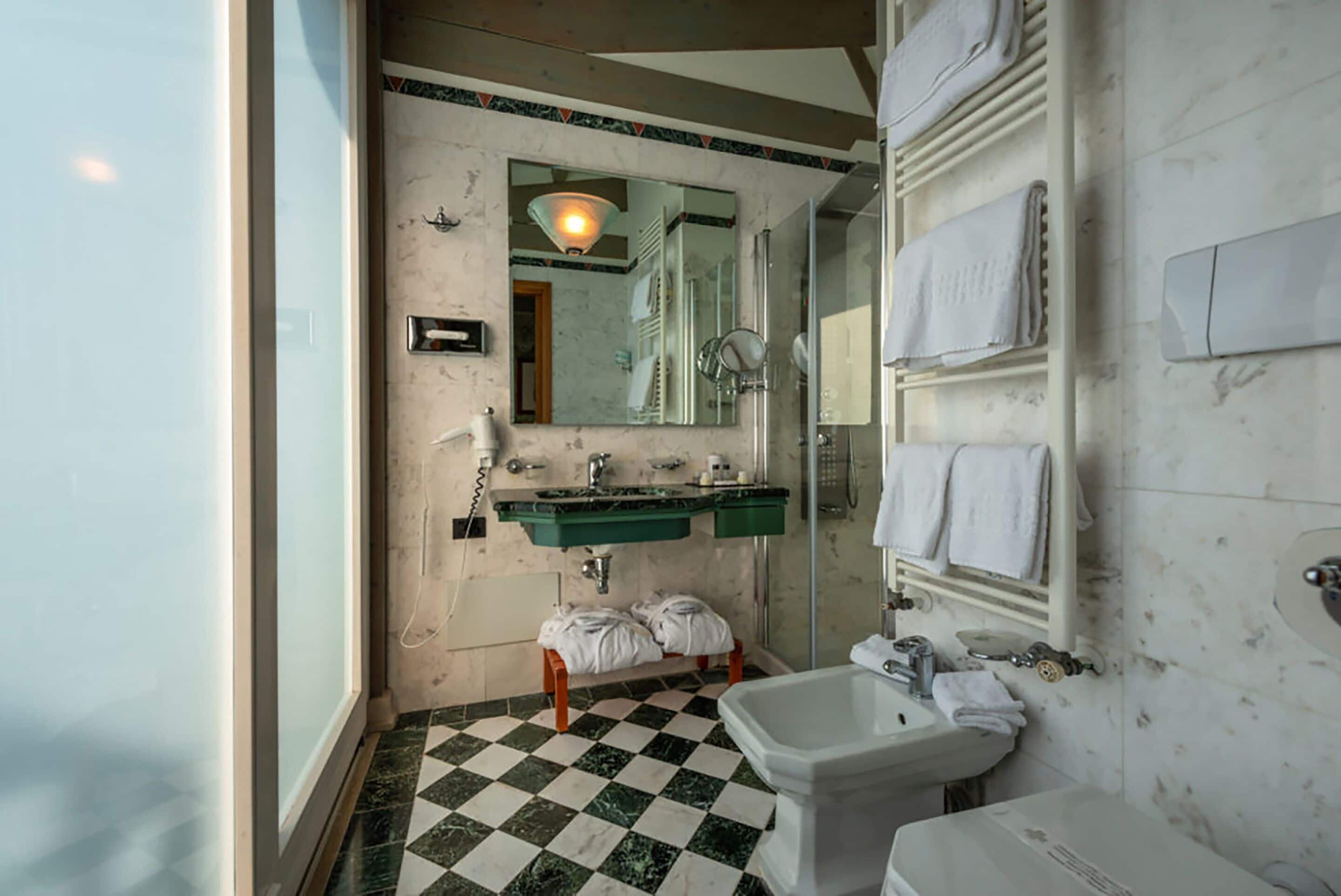Casa de banho com chão xadrez, lavatório verde, bidé branco e espelho sobre o lavatório.