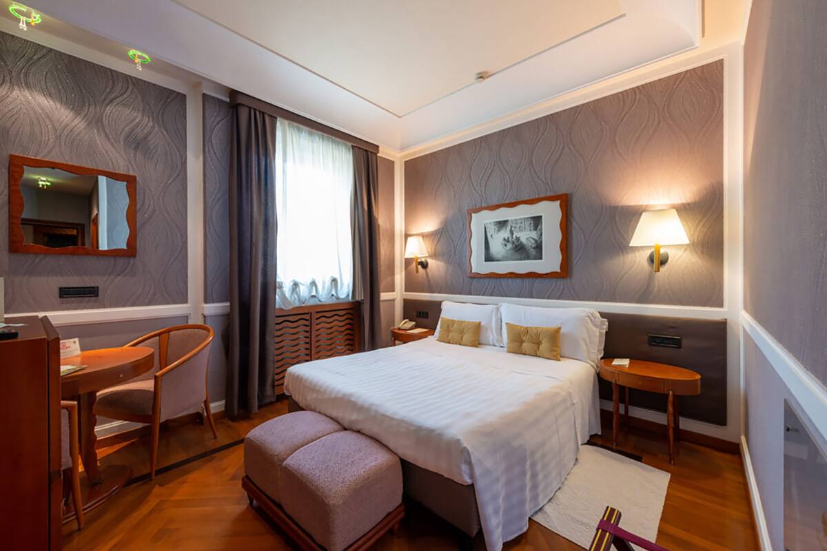 Una habitación de hotel con una cama grande, un escritorio, una silla, una mesita de noche y una lámpara.