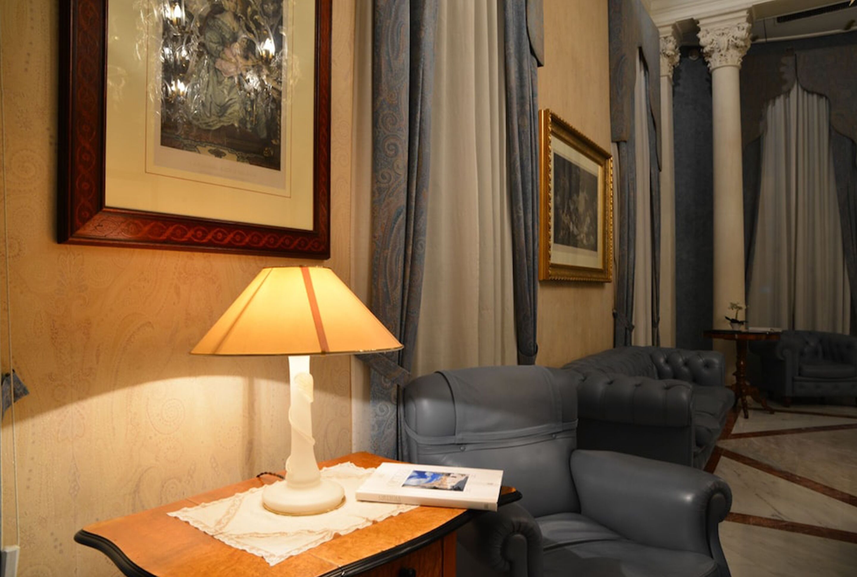 A room with a leather armchair, a table with a lamp, and framed artwork on the wall.