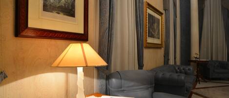 A room with a leather armchair, a table with a lamp, and framed artwork on the wall.