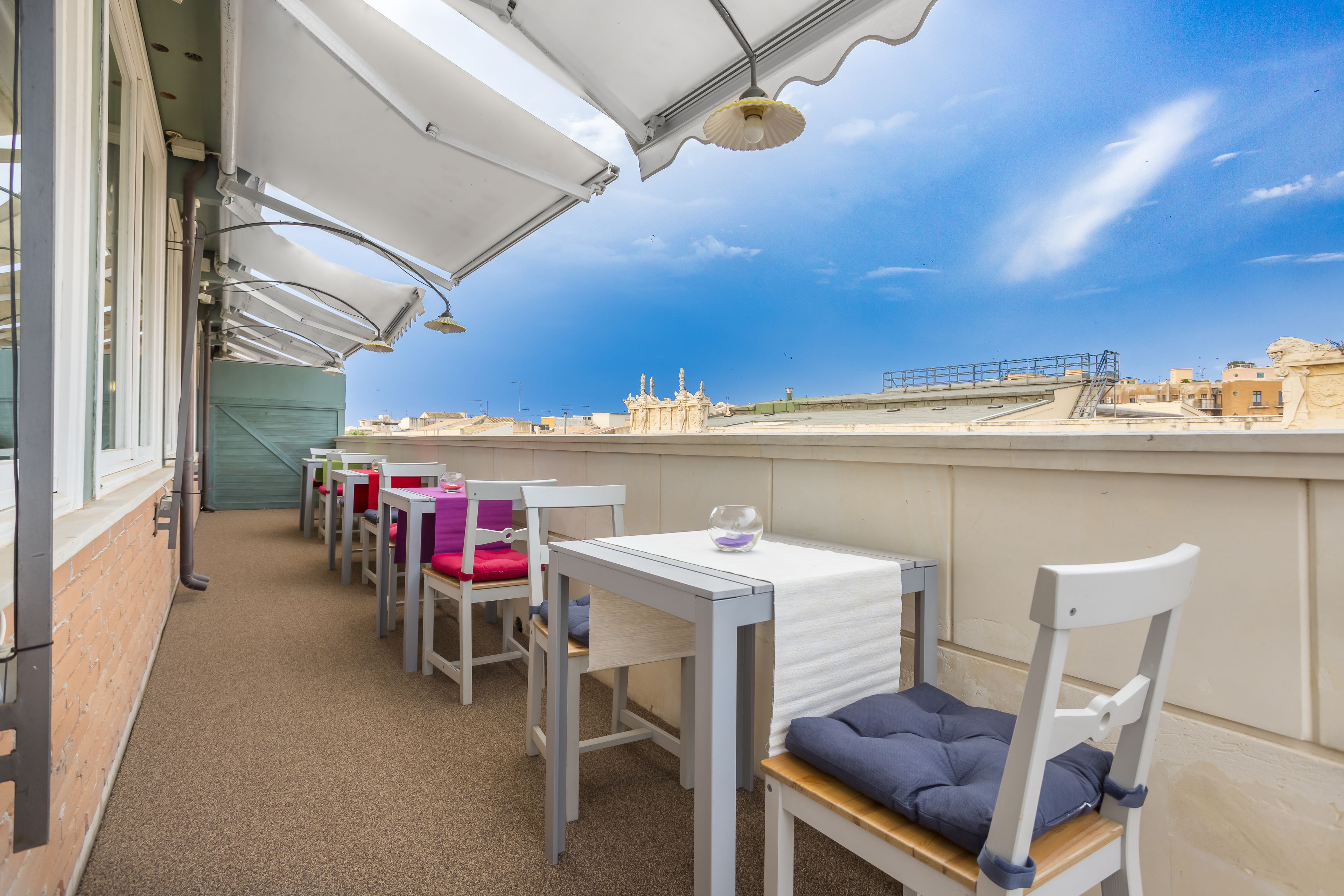 Une terrasse avec des tables et des chaises blanches, une vue dégagée sur le paysage urbain et un ciel bleu.