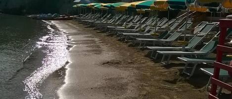 A beach with rows of sun loungers and umbrellas, a sandy shore, and a calm sea.