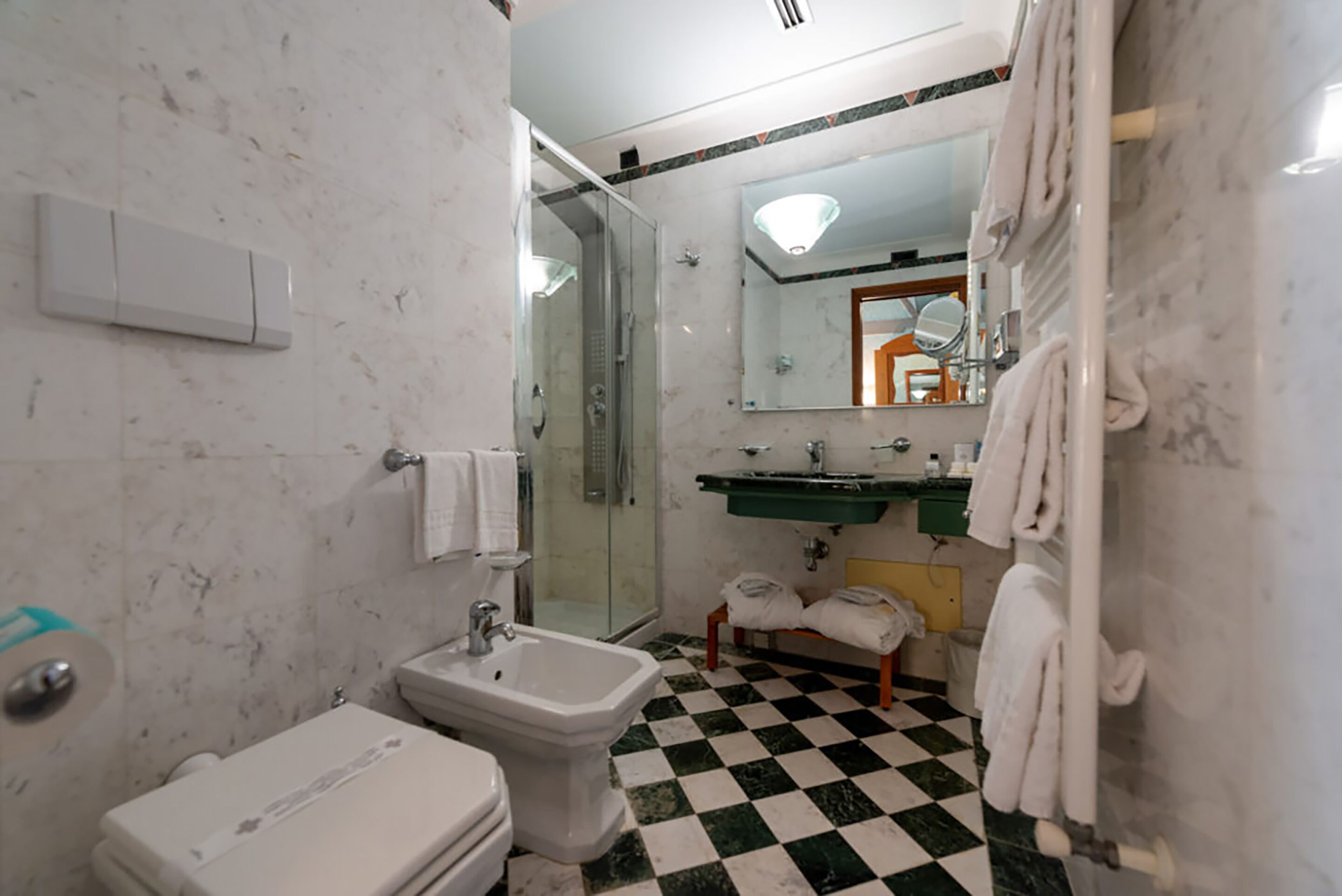 Un baño con inodoro, bidé, lavamanos y ducha con mampara de vidrio.