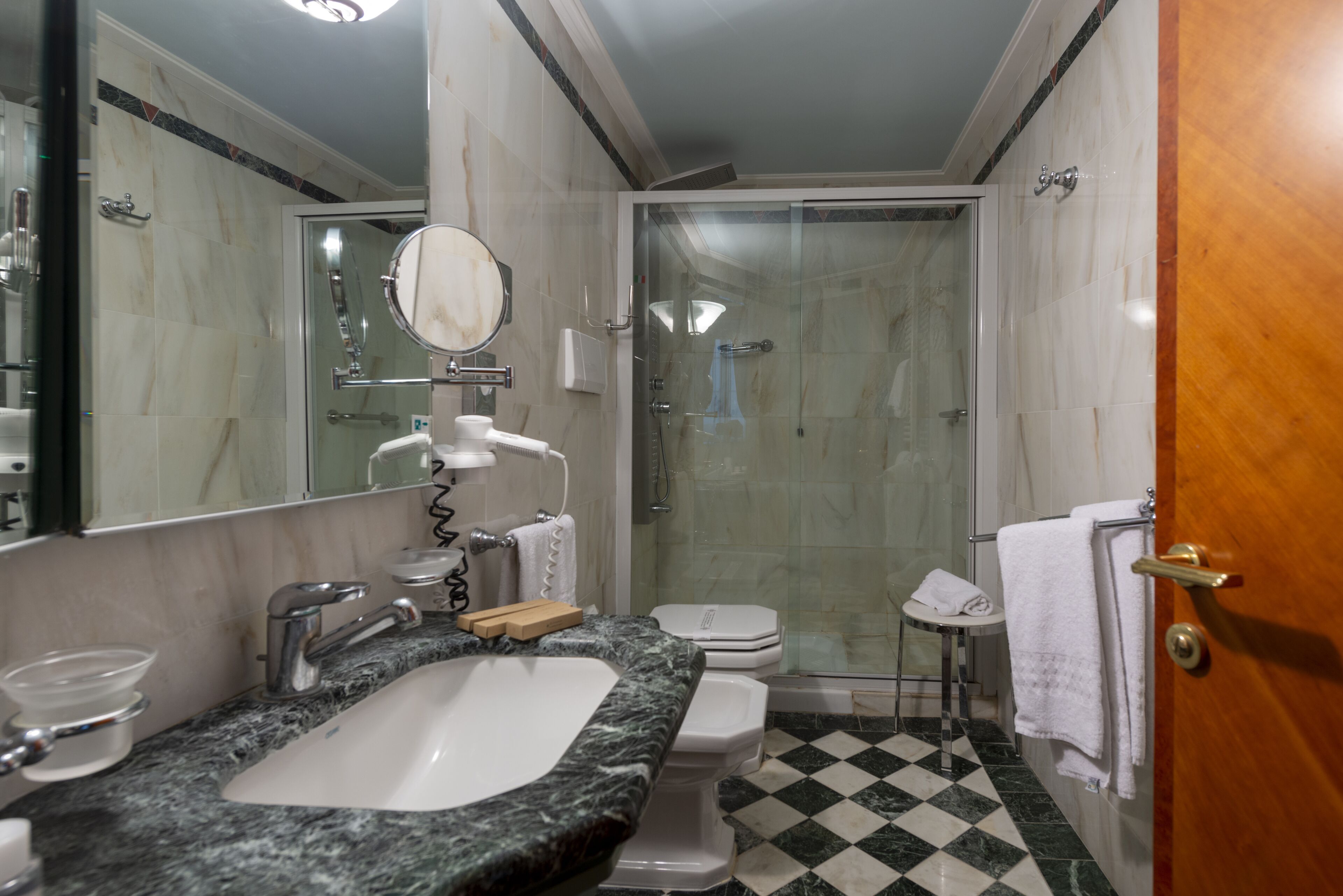 A bathroom with a marble sink, a toilet, a glass-enclosed shower, and a wooden door.