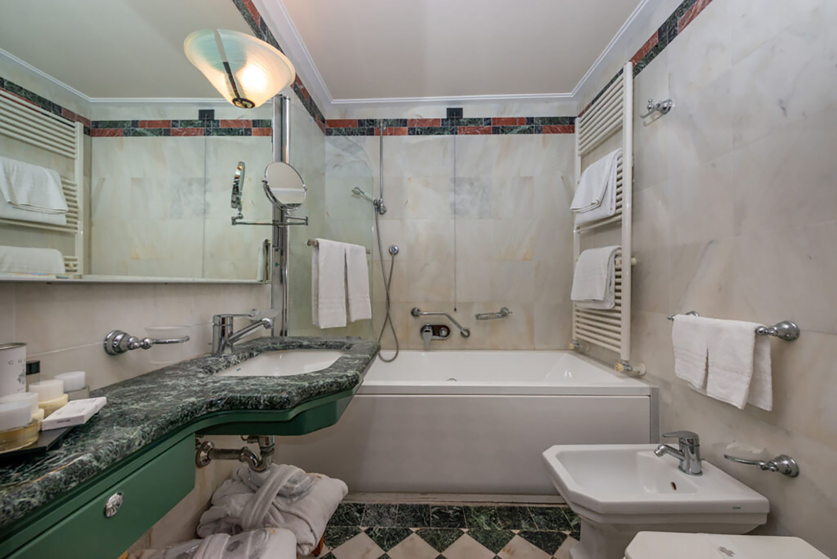 Un baño con bañera, lavamanos y espejo. Hay toallas colgadas en la pared y un cabezal de ducha sobre la bañera.