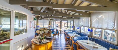 A restaurant with a checkered floor, wooden ceiling beams, and blue upholstered seating.