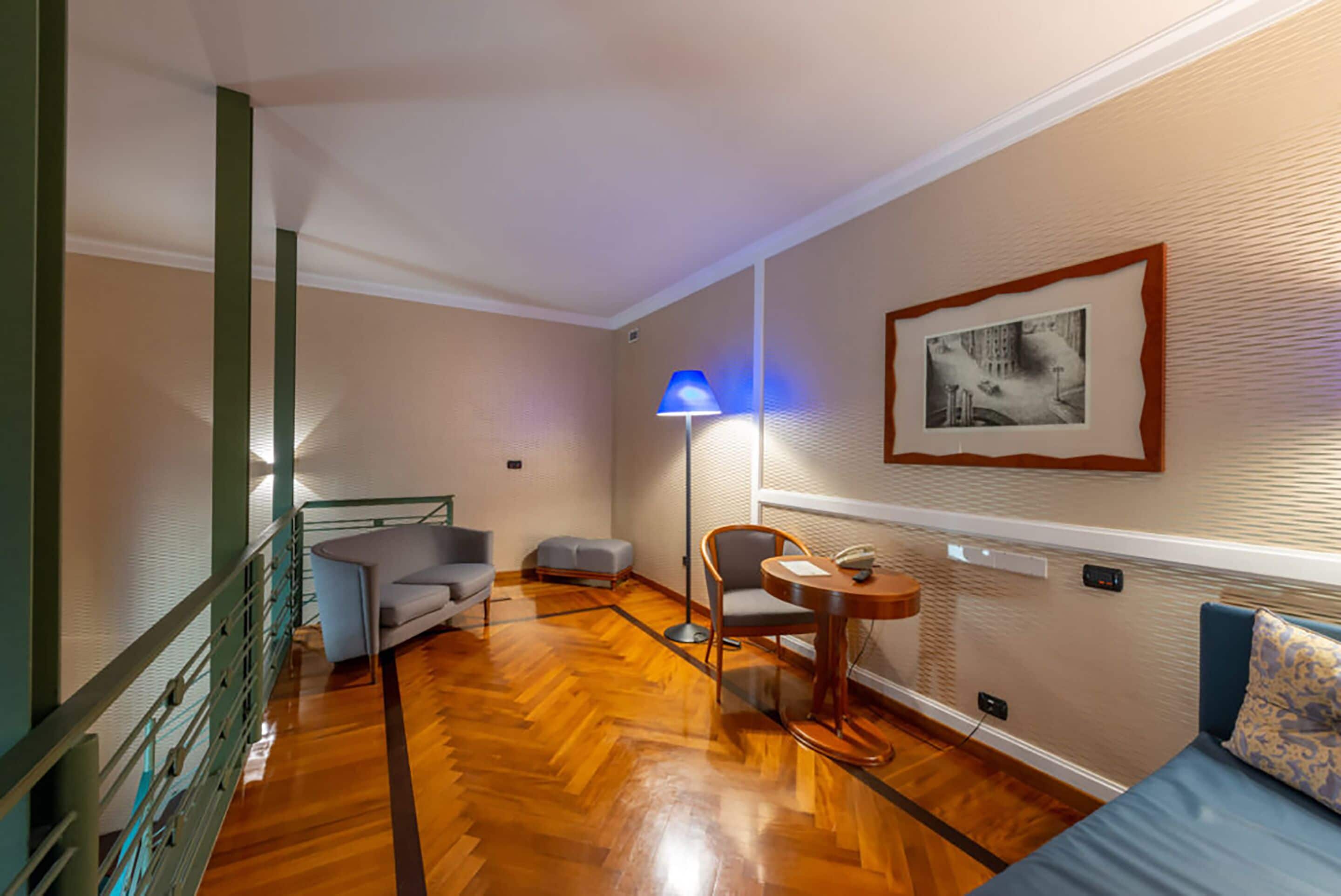 Ein Zimmer mit Holzboden, einer Couch, einem Sessel, einem kleinen Tisch und einer Lampe.