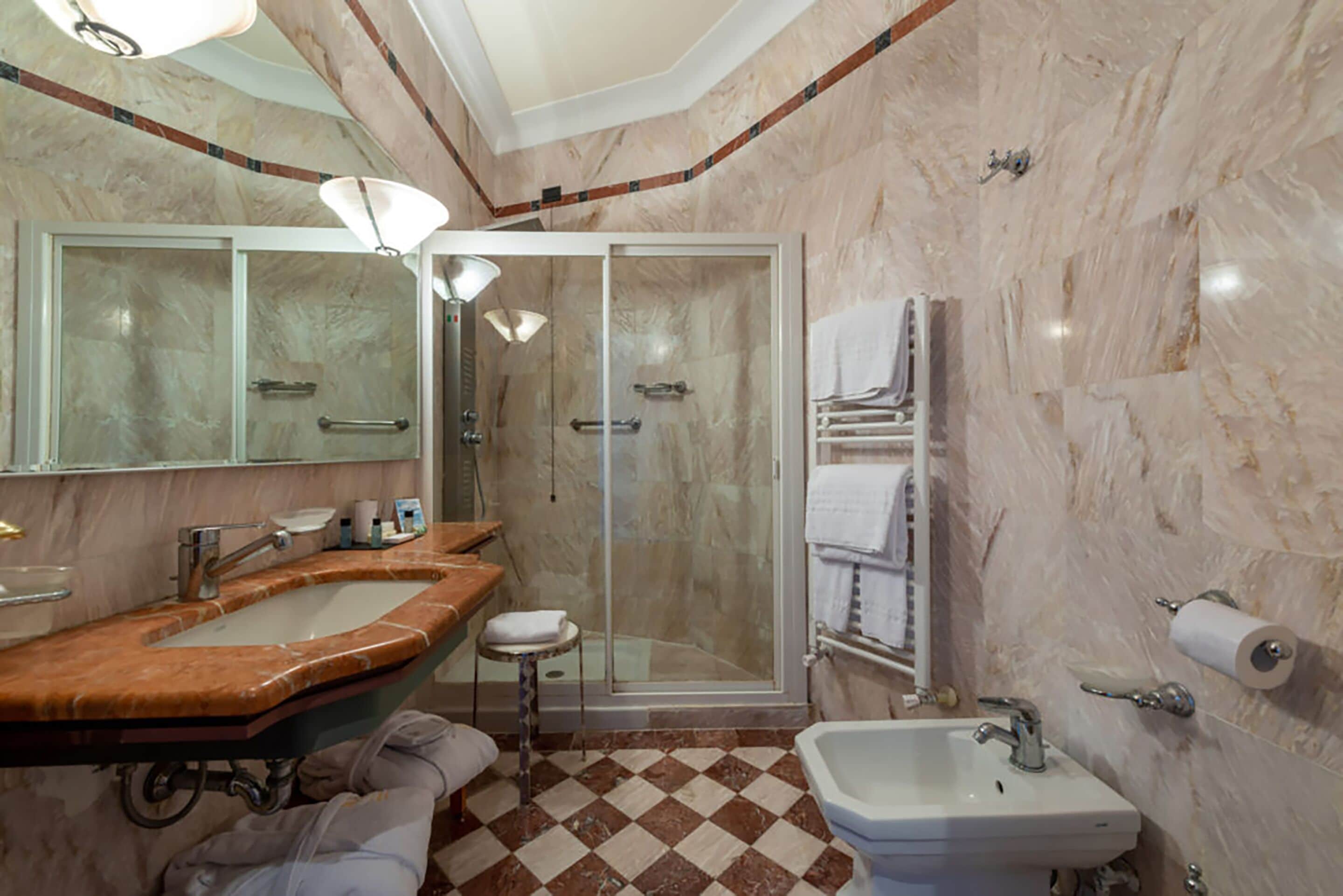 A bathroom with a marble floor, a sink, a mirror, a shower, and a towel rack.