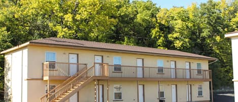 Um motel de dois andares com uma escadaria central, várias portas e estacionamento.