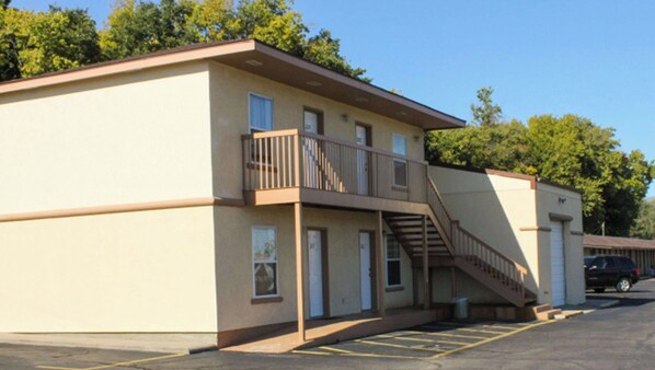 A two-story motel with a balcony on the second floor, a parking lot, and a clear sky.
