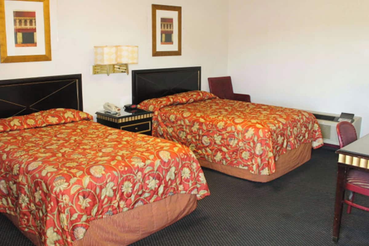 A hotel room with two beds, a desk, a chair, and a lamp.