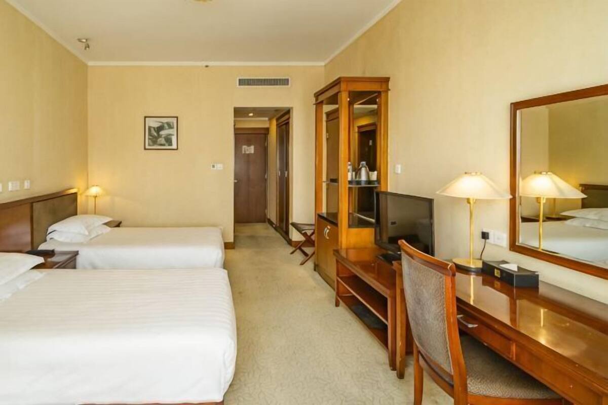 Une chambre d’hôtel avec deux lits, un bureau avec une chaise, une télévision, un miroir et une armoire.