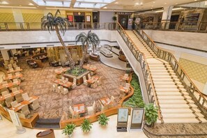 A hotel lobby with a central seating area, multiple dining tables, a staircase, and a palm tree. - New Century Hotel Ninghai (Ningbo)
