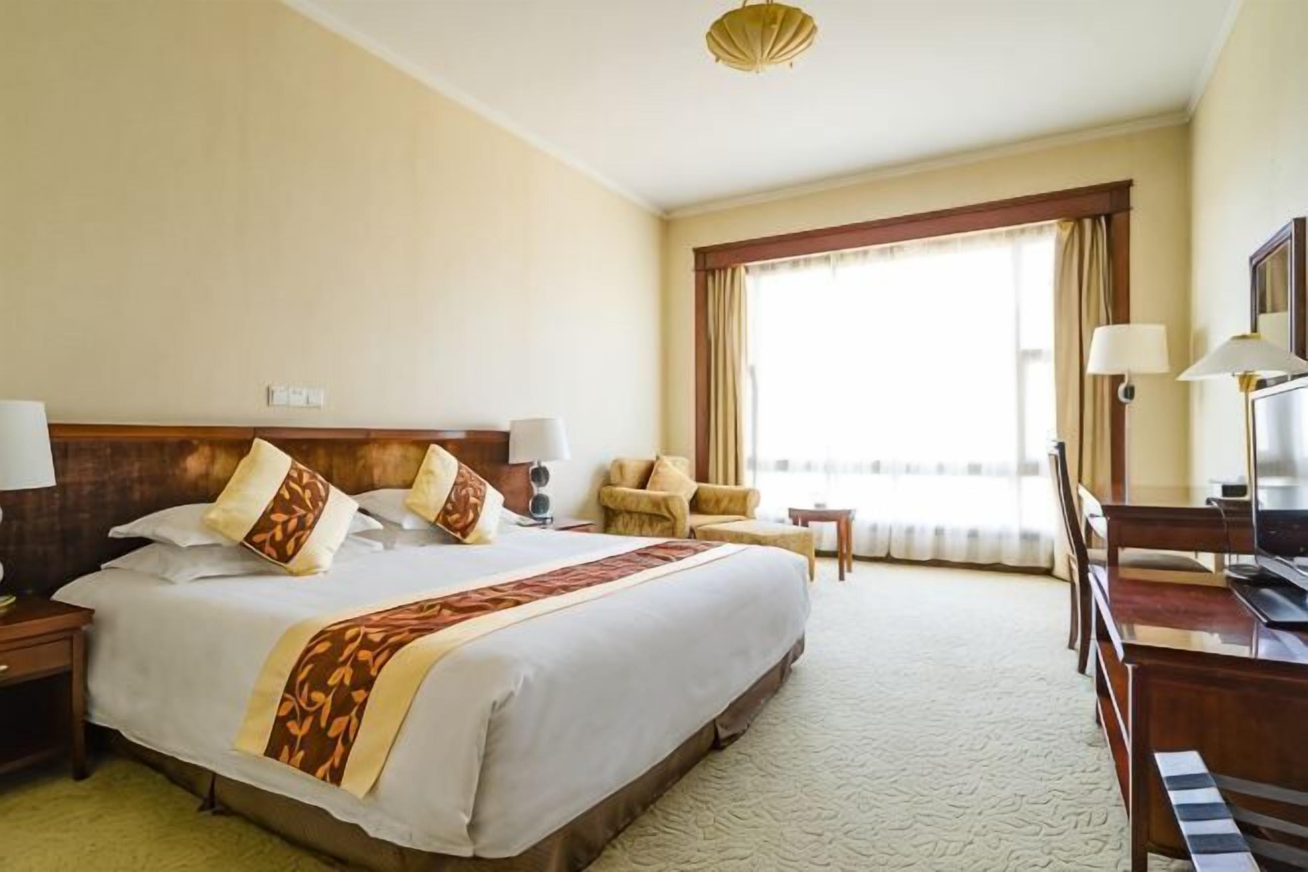 Ett hotellrum med en stor säng, ett skrivbord, en stol, en tv och ett fönster med gardiner.