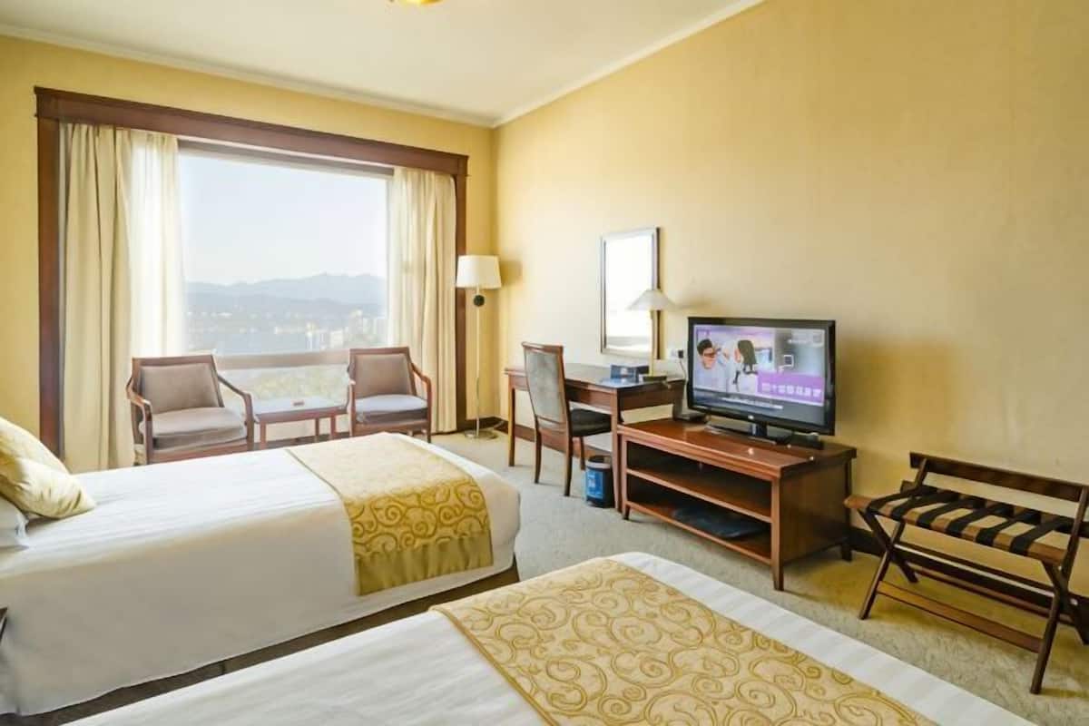Une chambre d’hôtel avec deux lits, un bureau, une télévision, une chaise et une vue sur la ville.