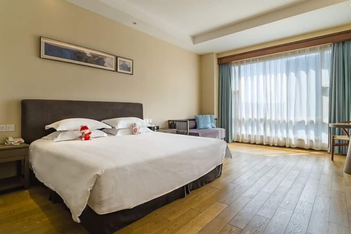 Une chambre d’hôtel avec un grand lit, une table de chevet, une chaise, une fenêtre avec des rideaux et un tableau au mur.
