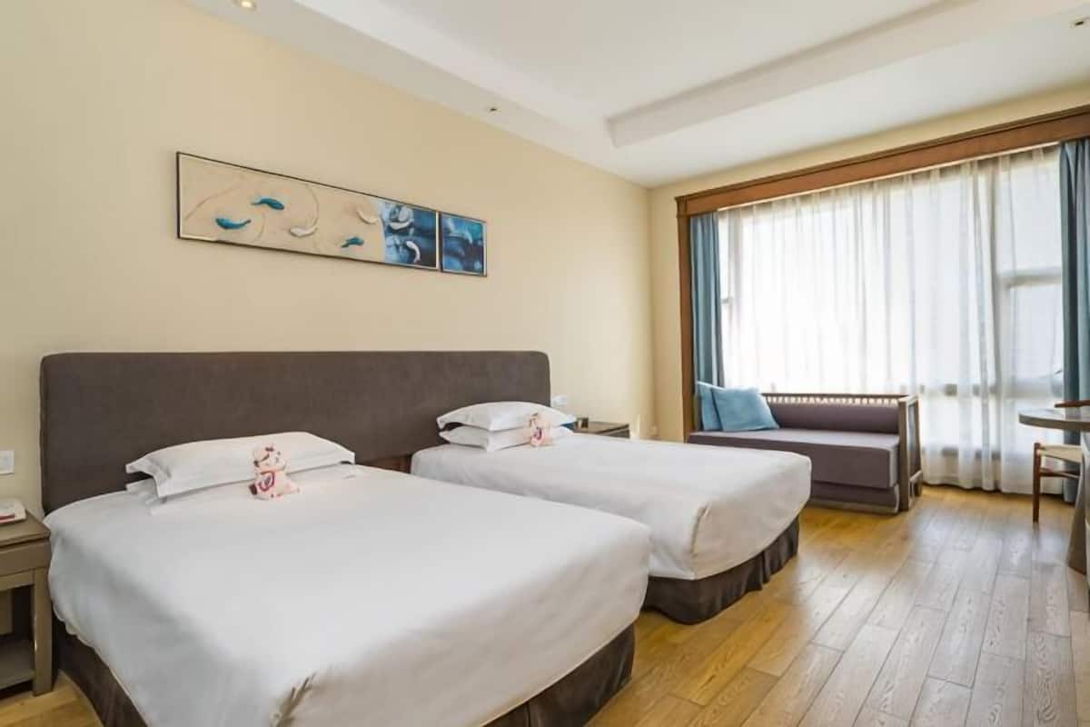 Une chambre d’hôtel avec deux lits, un canapé, une petite table et une fenêtre avec des rideaux.