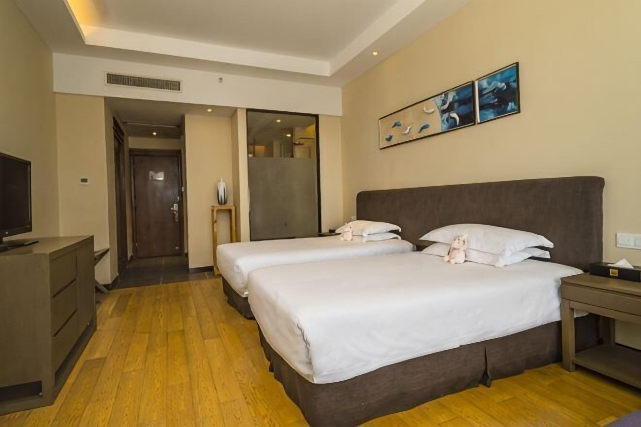 Una habitación de hotel con dos camas, televisión, escritorio y un cuadro en la pared.