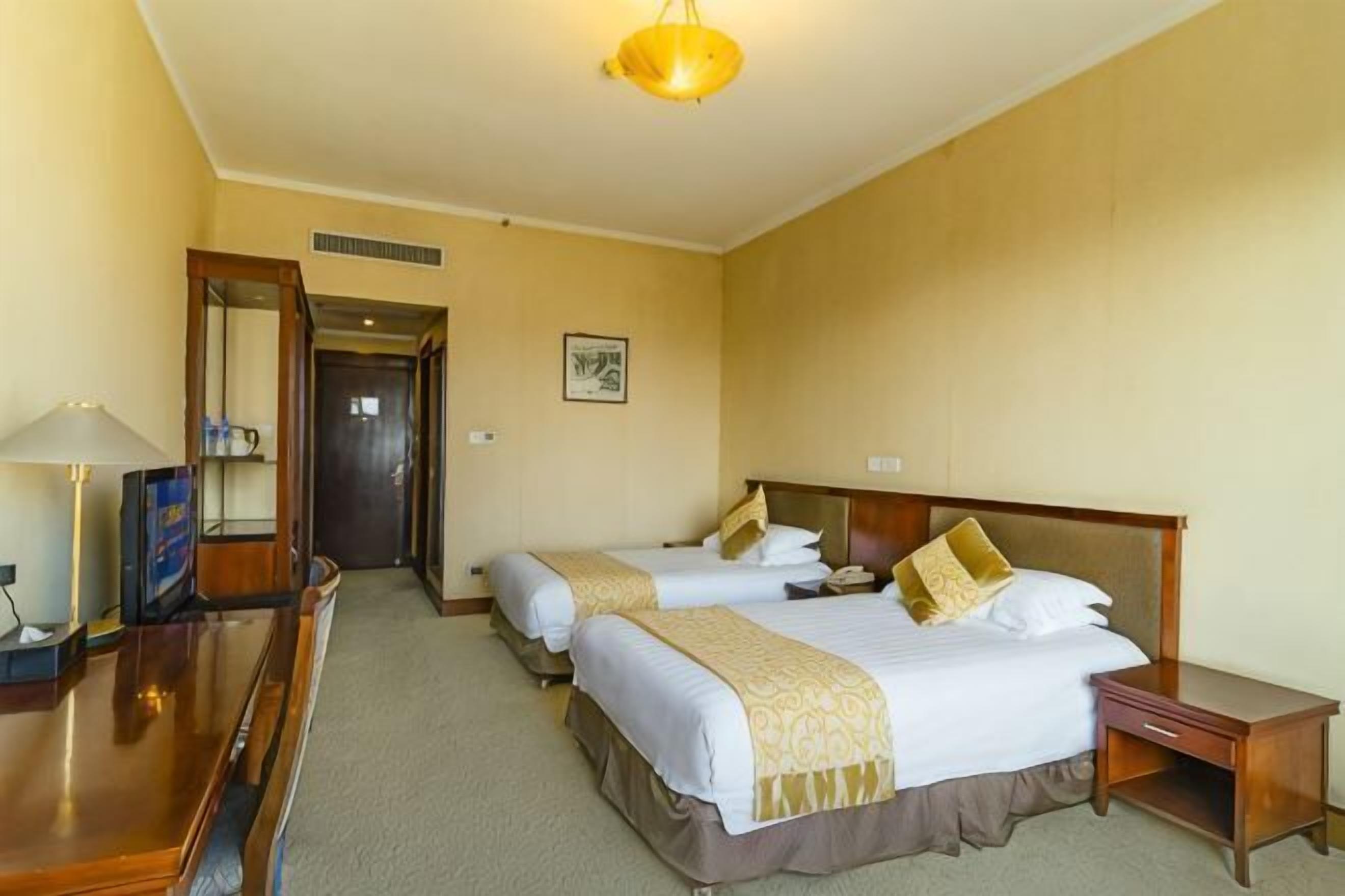 Una habitación de hotel con dos camas, un escritorio, una silla, una lámpara y un espejo.