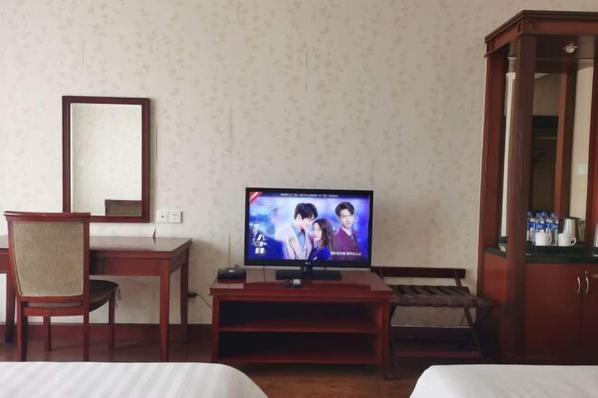 Une chambre d’hôtel équipée d’une télévision posée sur un meuble en bois, d’un bureau avec une chaise, d’un lit et d’une armoire.