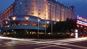 Un hotel de varios pisos con fachada curva, ventanas iluminadas y una bandera en el techo.