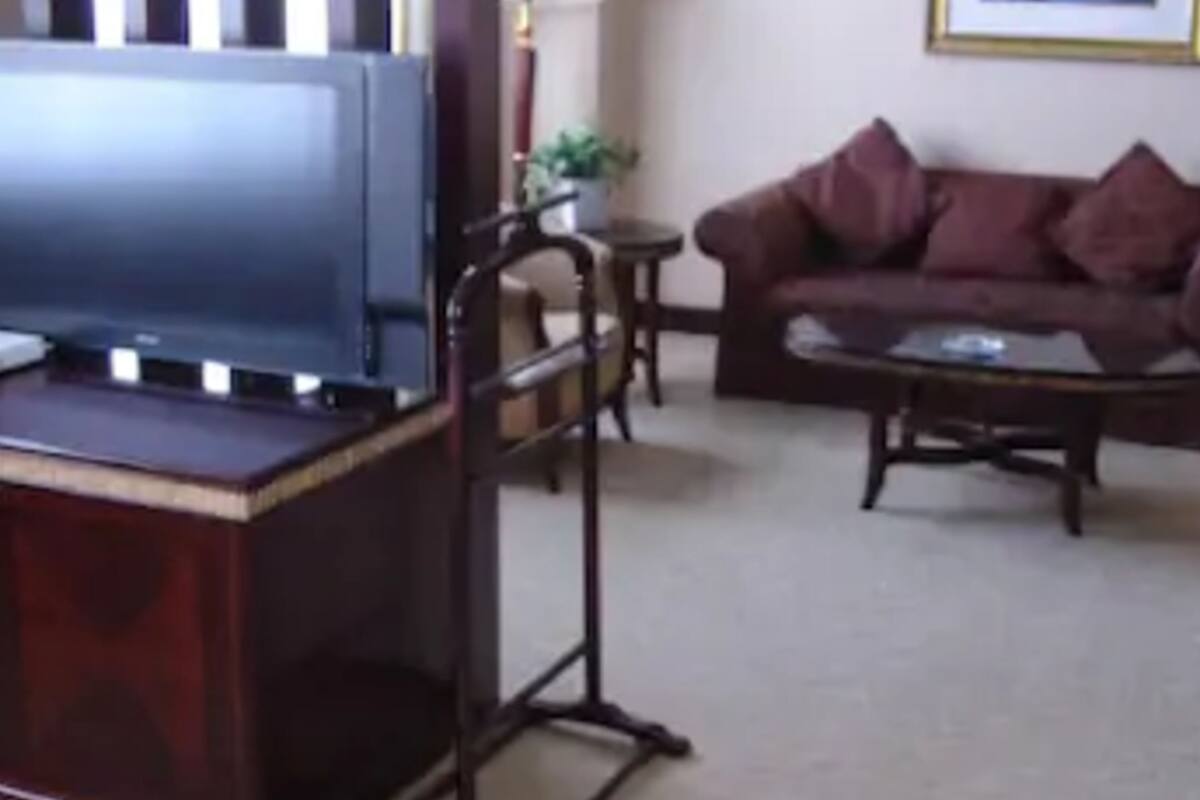 Uma sala de estar com um rack de madeira escura, um sofá com várias almofadas, uma mesinha de centro redonda e um quadro na parede.