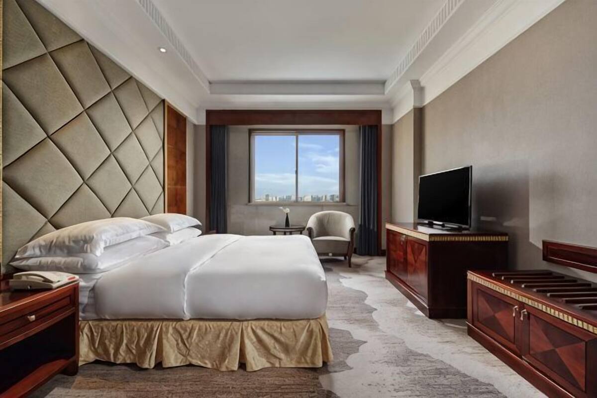 Quarto de hotel com uma cama grande, televisão, escrivaninha e vista da cidade.