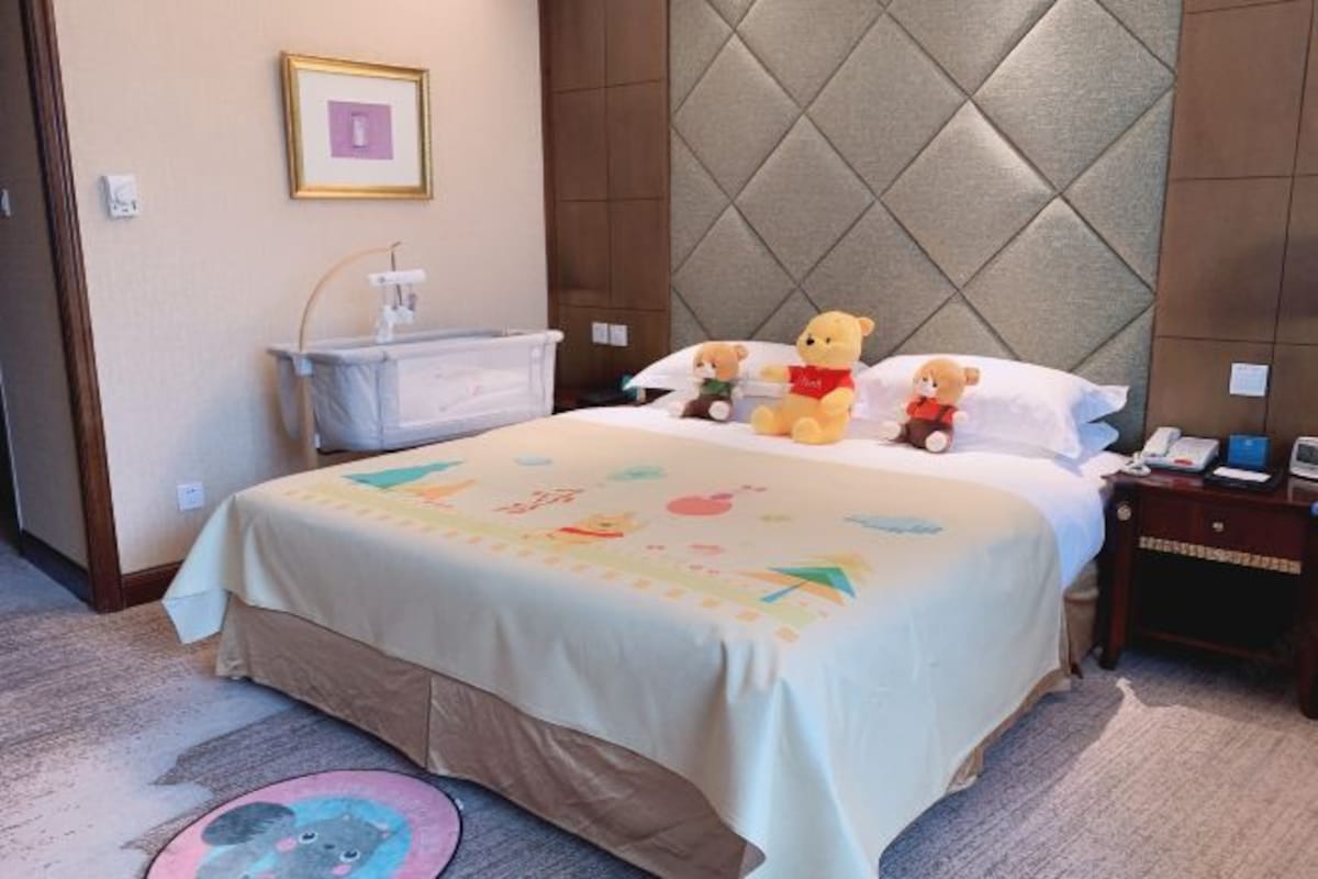 A hotel room with a bed, a bedside table, a nightstand, a wall-mounted telephone, and a picture frame on the wall.