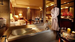 A hotel room with a large bathtub, a mirror, a robe hanging, and a table with toiletries and candles. - New Century Grand Hotel Xuzhou (Xuzhou)