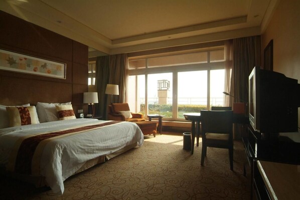 A hotel room with a large bed, a desk, a chair, a television, and a window with a view.