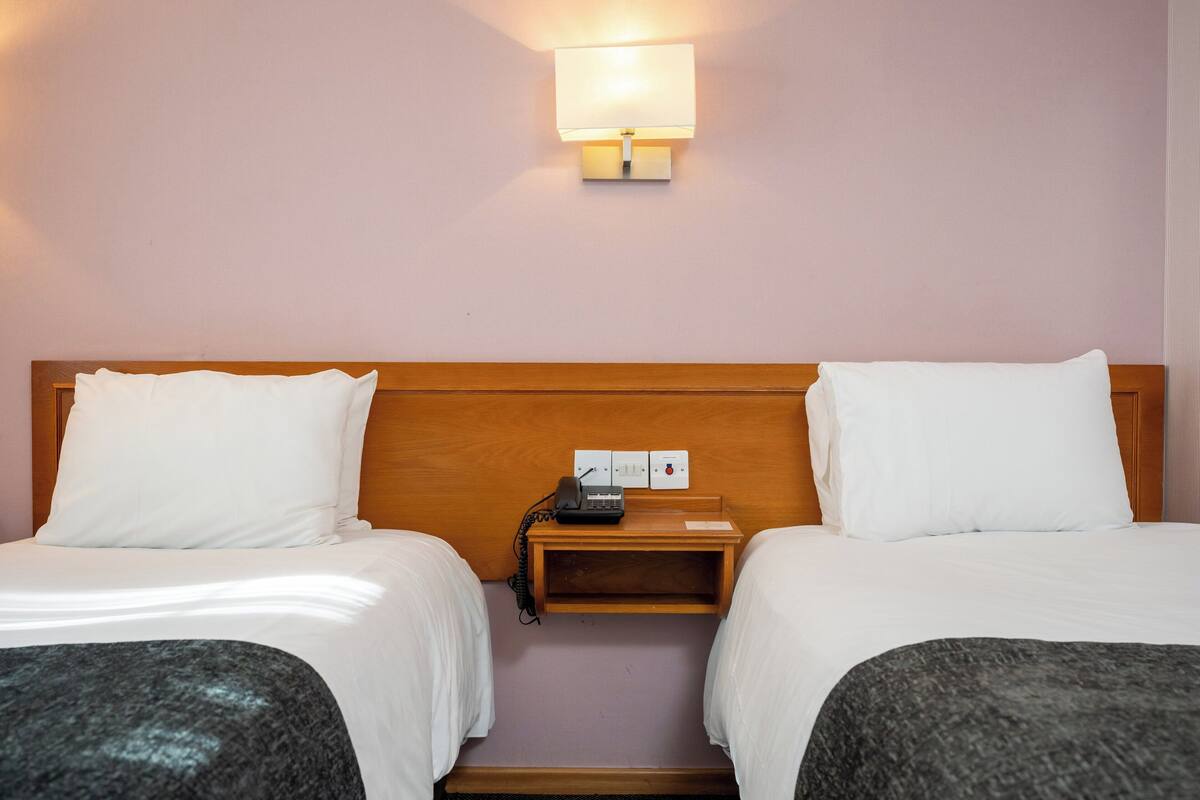 A hotel room with two beds, a bedside table with a lamp, and a phone.