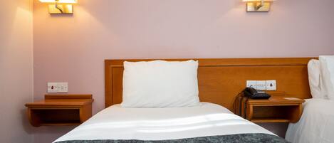 A hotel room with a wooden headboard, a white bedspread, a gray throw blanket, two bedside tables with lamps, and a telephone.