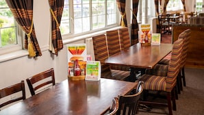 A restaurant with a long wooden table, striped booth seating, and a menu stand. - Bridge Inn by Greene King Inns (Bristol)