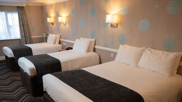 A hotel room with two beds, a patterned carpet, and wall-mounted lamps. - Bridge Inn by Greene King Inns (Bristol)