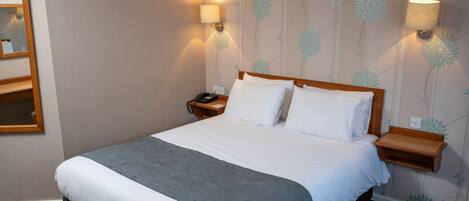 A neatly made bed with white and grey bedding, two bedside lamps, and a nightstand with a phone.
