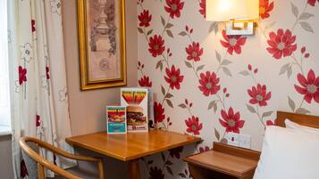 A hotel room with a wooden table, a framed picture on the wall, a floral wallpaper, and a breakfast menu on the table.