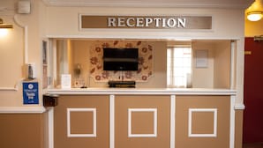 A reception area with a sign labeled "RECEPTION," a flat-screen TV mounted above a floral-patterned wall, and a hand sanitizer station. - Bridge Inn by Greene King Inns (Bristol)