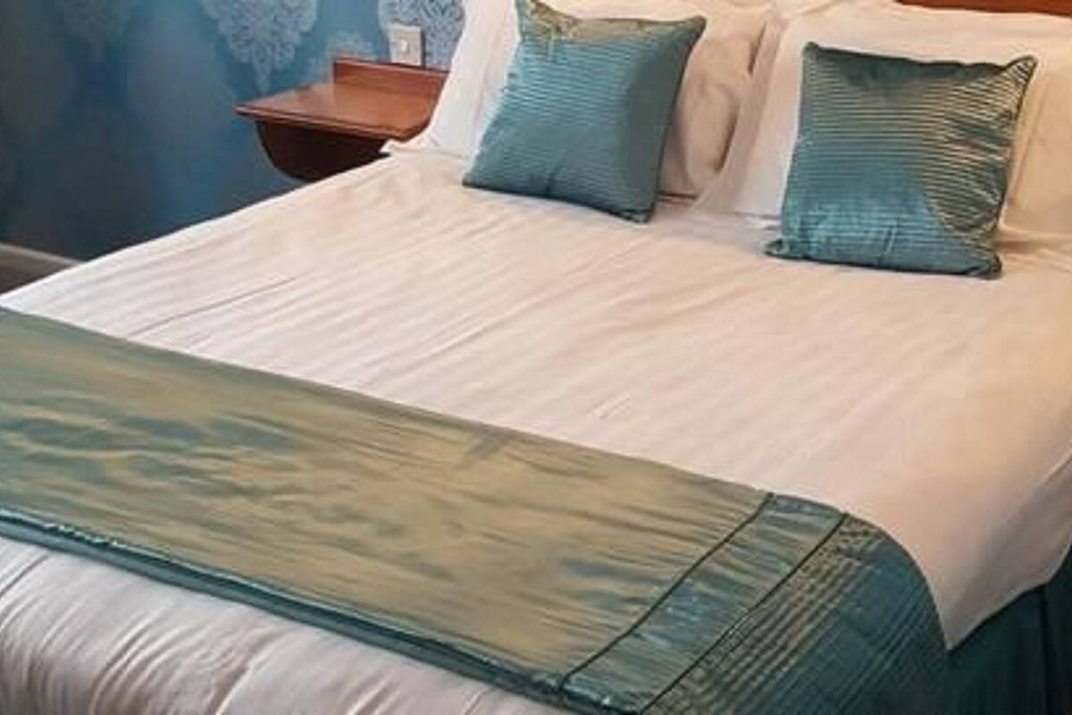 A bed with a white and teal bedspread, two teal pillows, and a teal throw blanket.
