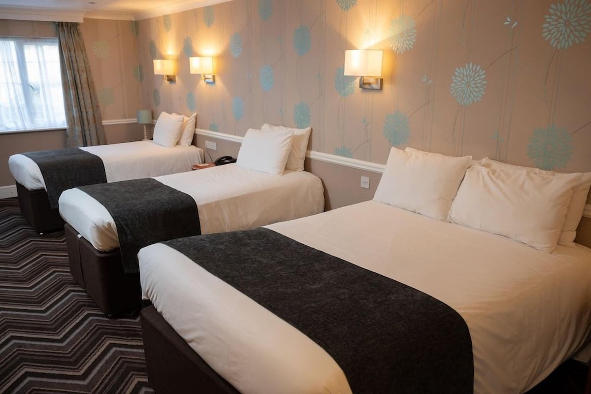 A hotel room with two beds, a patterned wall, and a window with curtains.