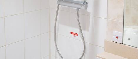 A shower with a handheld showerhead, a wall-mounted faucet, and a control panel.