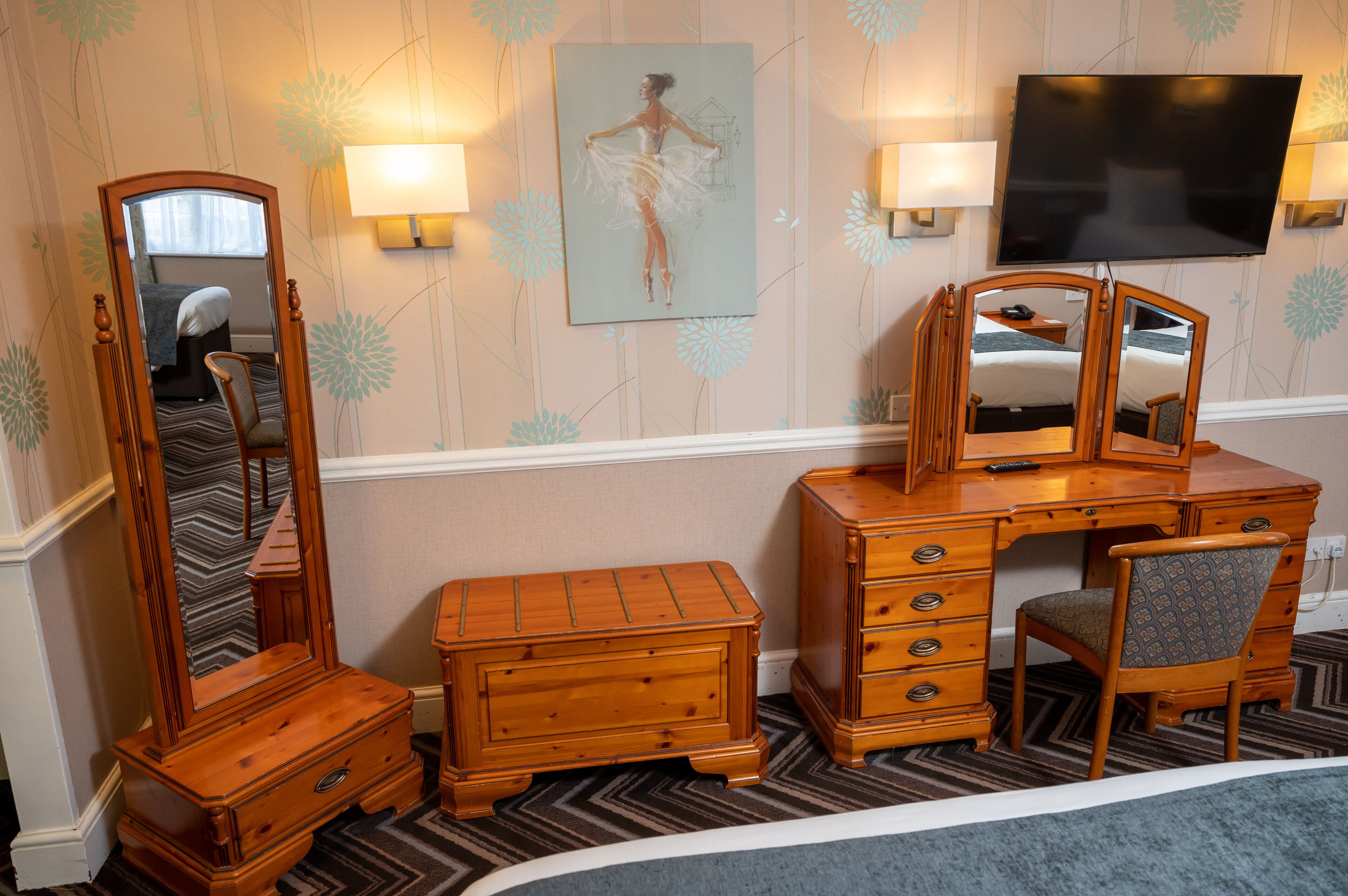 A hotel room with a wooden dresser, a mirror, a television, and a bed.